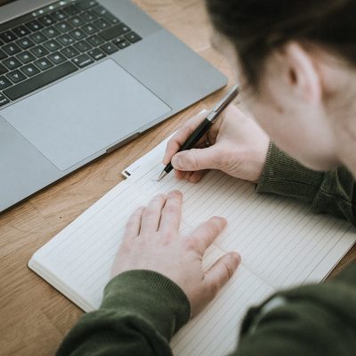 Frau schreibt auf Block mit Computer im Blick
