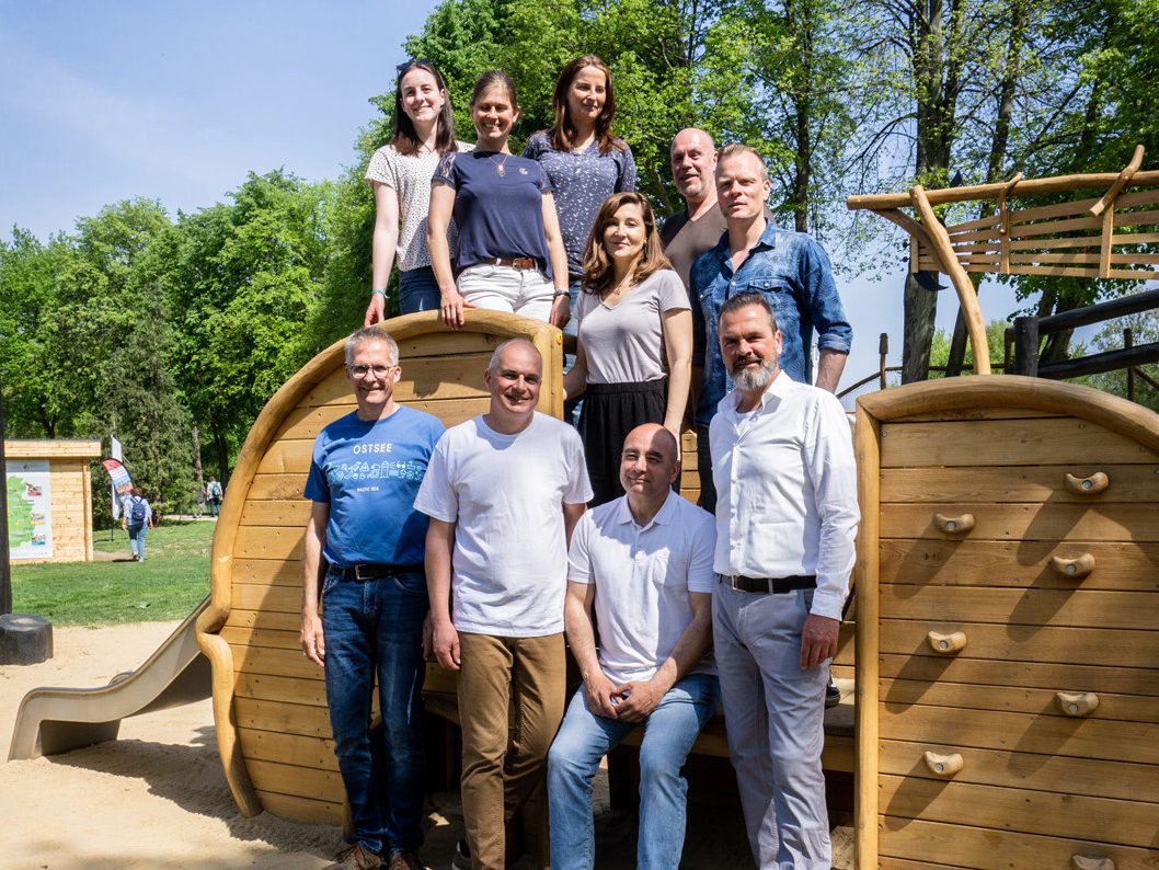 Team SIK-Holz mit Geschäftsführer Marc Oelker in der Gruppe stehend vor einem Spielplatzgerät