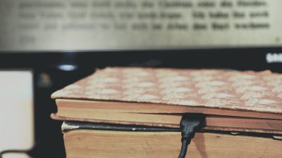 Ladekabel steckt zwischen den Seiten eines alten Buches. Im Hintergrund erscheint der TExt des Buches auf einem Bildschirm