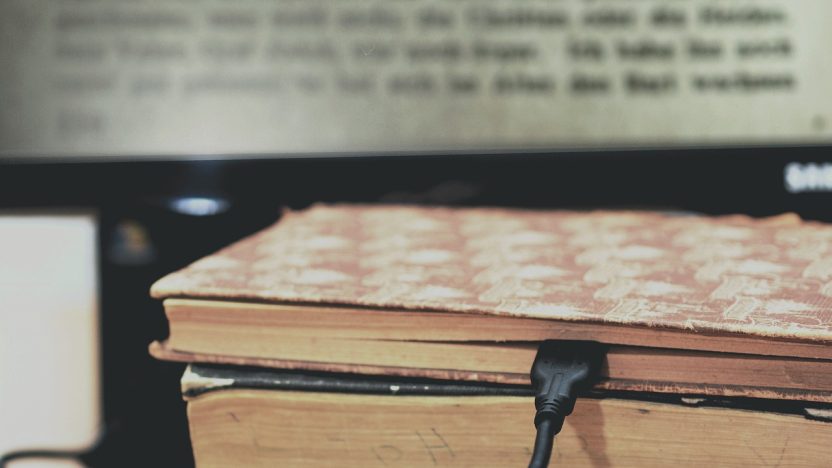 Ladekabel steckt zwischen den Seiten eines alten Buches. Im Hintergrund erscheint der TExt des Buches auf einem Bildschirm