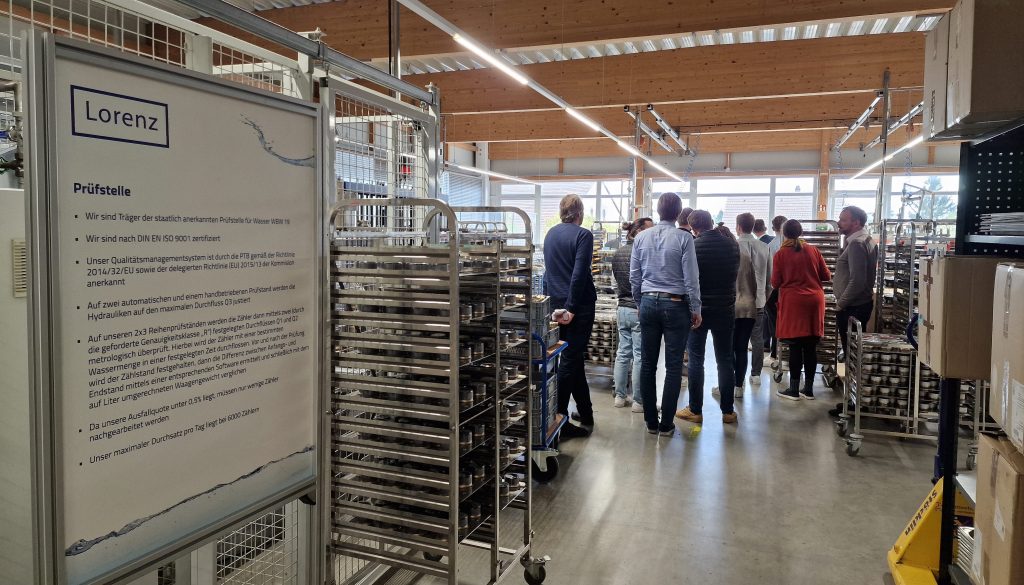 eine Gruppe von Menschen steht in einer Produktionshalle für die Herstellung von Wasserzählern